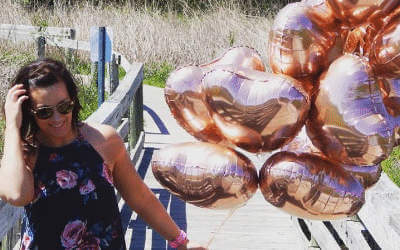 A girl carrying a big bunch of metallic pink balloons